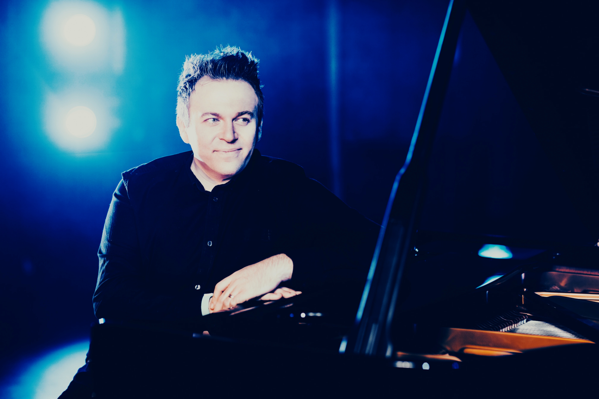 Musical Theatre lecturer Ryan Murphy leaning on a piano. The background shows stage lights.