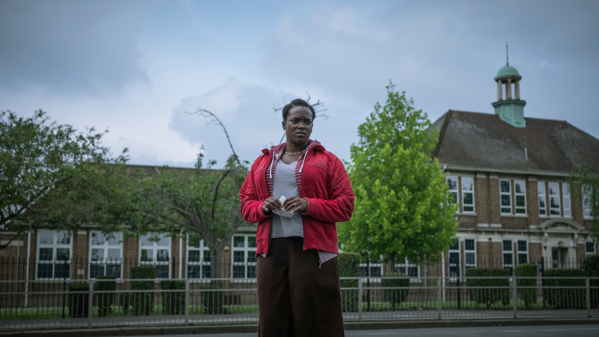 Still from 'His House' showing woman clutching letter in front of building
