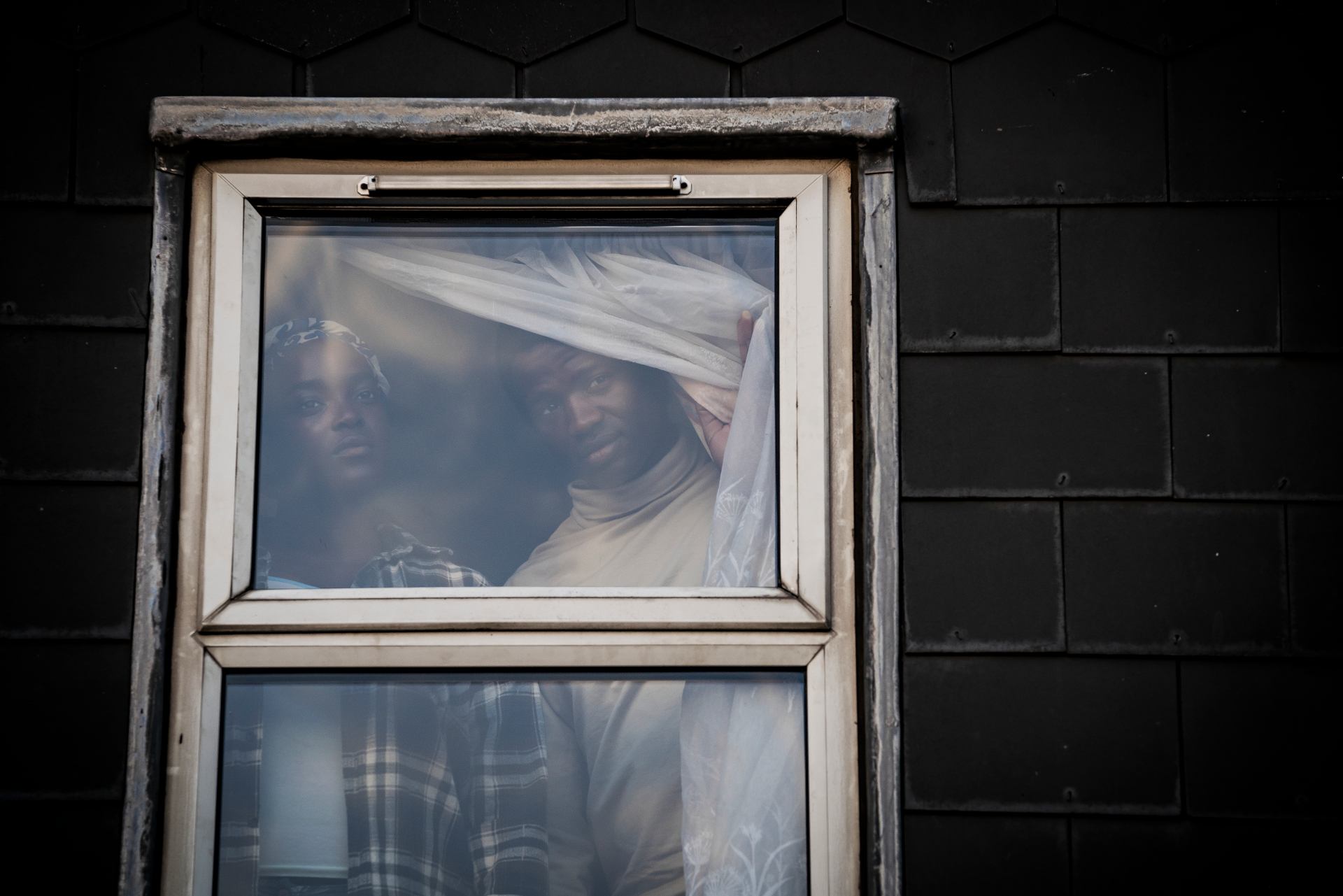 Still from 'His House' showing man and woman looking out of window